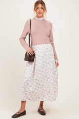 woman wearing a pink long sleeve maternity top and a floral print maxi dress, holding a brown bag and smiling