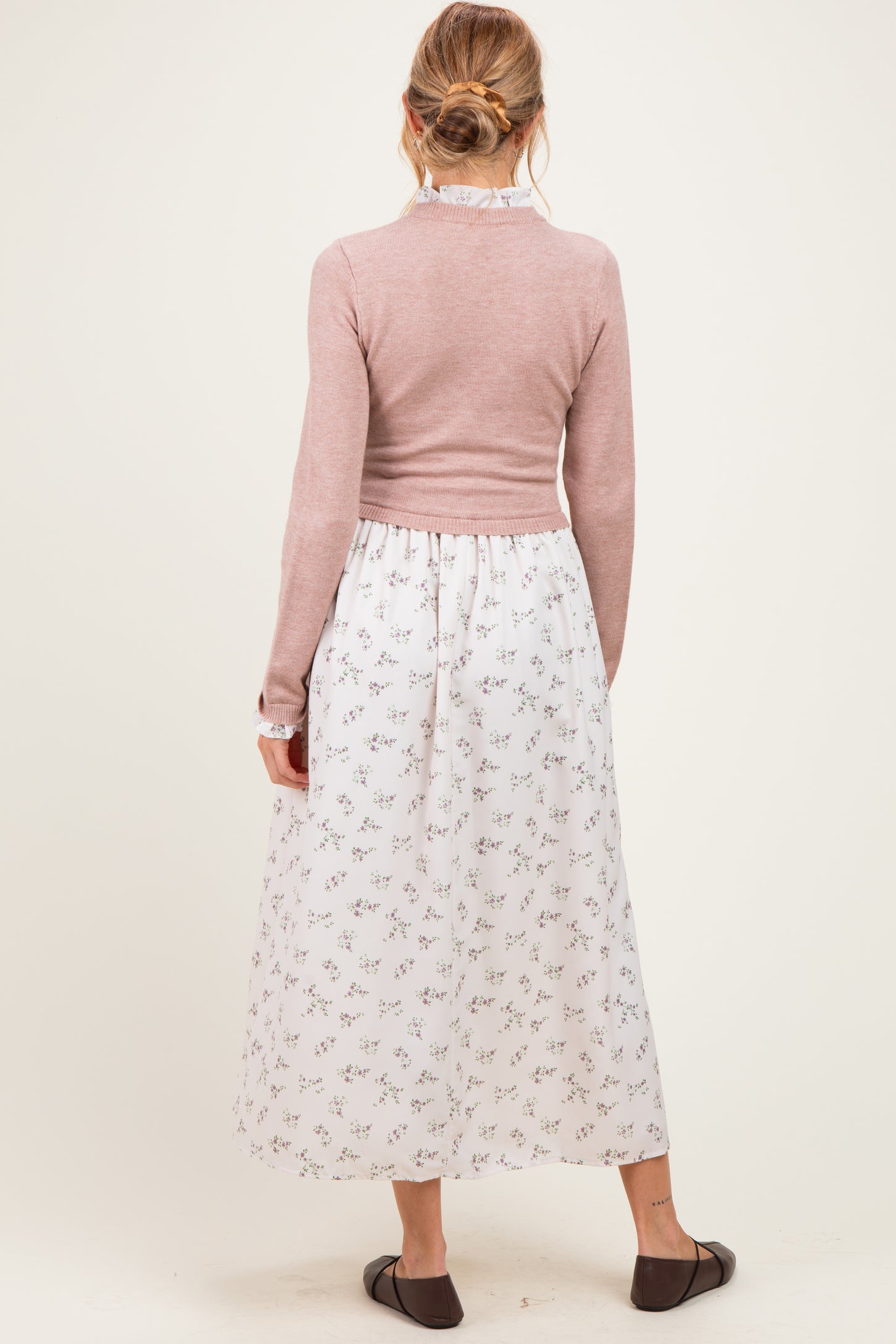 woman wearing a pink long sleeve maternity sweater and a white floral maxi skirt with a gathered waist, showing her baby bump