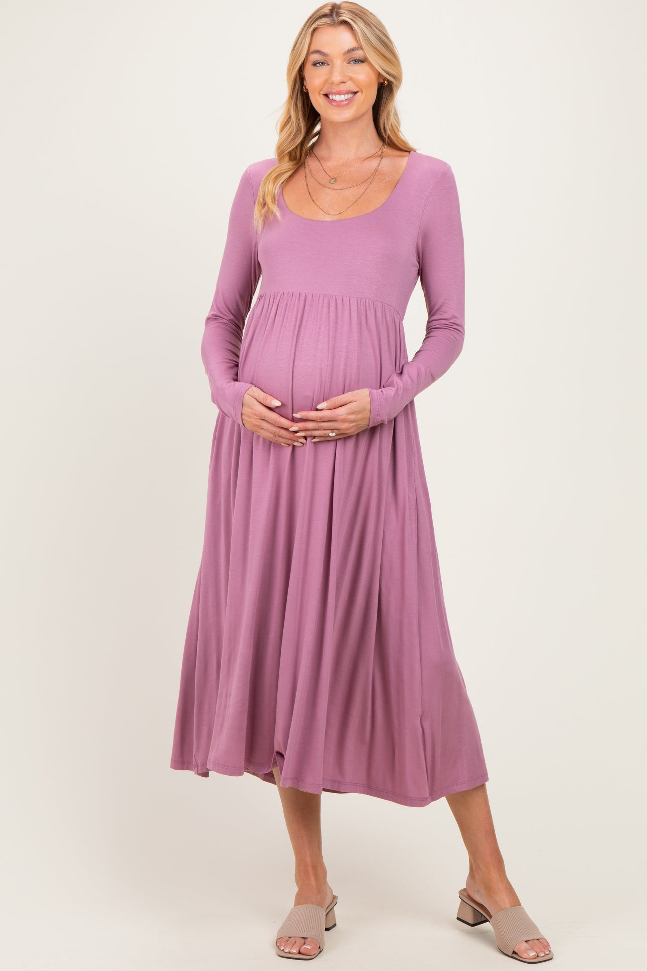 woman wearing a lavender long sleeve maternity dress with a flowing skirt and holding her baby bump