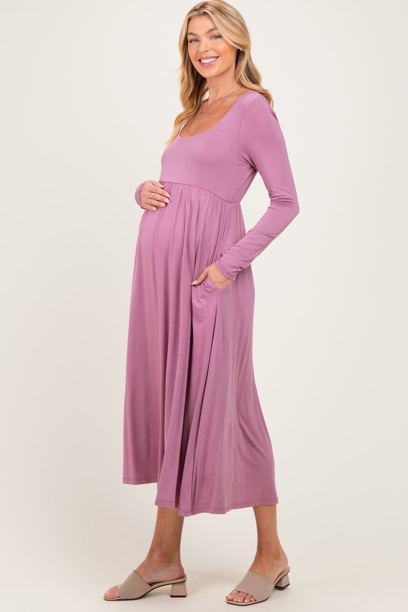 woman wearing a lilac long sleeve maternity dress with pockets and gently holding her baby bump