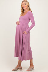 woman wearing a lilac long sleeve maternity dress with pockets and gently holding her baby bump