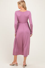 woman wearing a mauve long sleeve maternity dress with a fitted waist and flowing skirt
