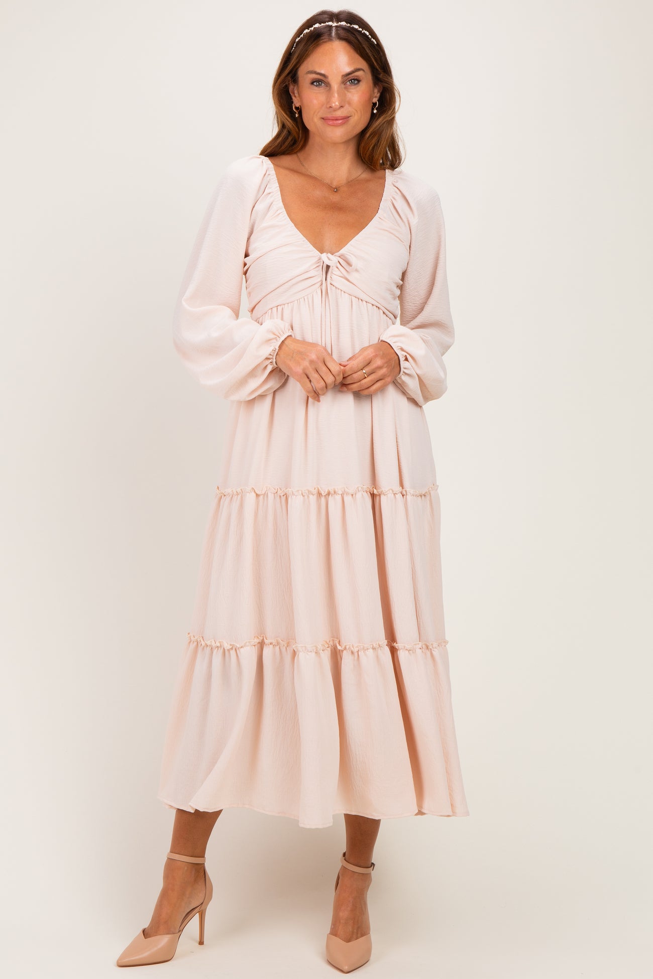 woman wearing a blush pink long sleeve midi dress with a gathered bodice and tiered skirt, standing on a neutral background