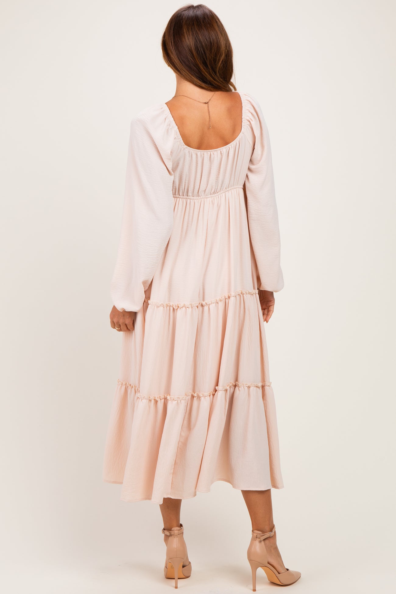 woman wearing a blush pink long sleeve tiered maxi dress, showing the back view with a scoop neckline
