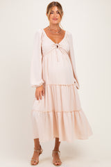 woman wearing a light pink maternity dress with a tie-front detail and tiered skirt, showcasing her baby bump