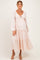 woman wearing a light pink maternity dress with a tie-front detail and tiered skirt, showcasing her baby bump