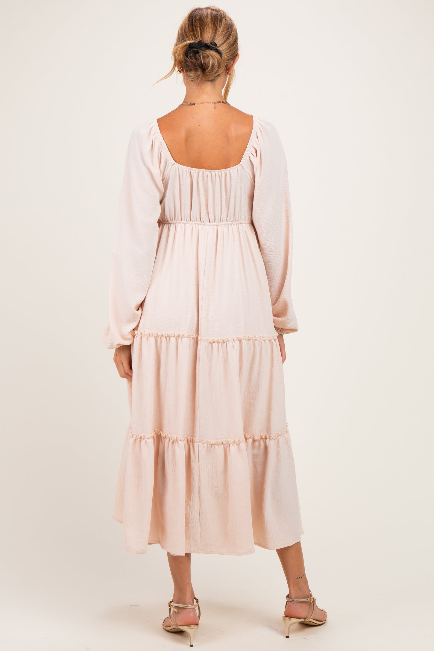 woman wearing a pale pink three-tiered maternity dress with long sleeves and a square neckline