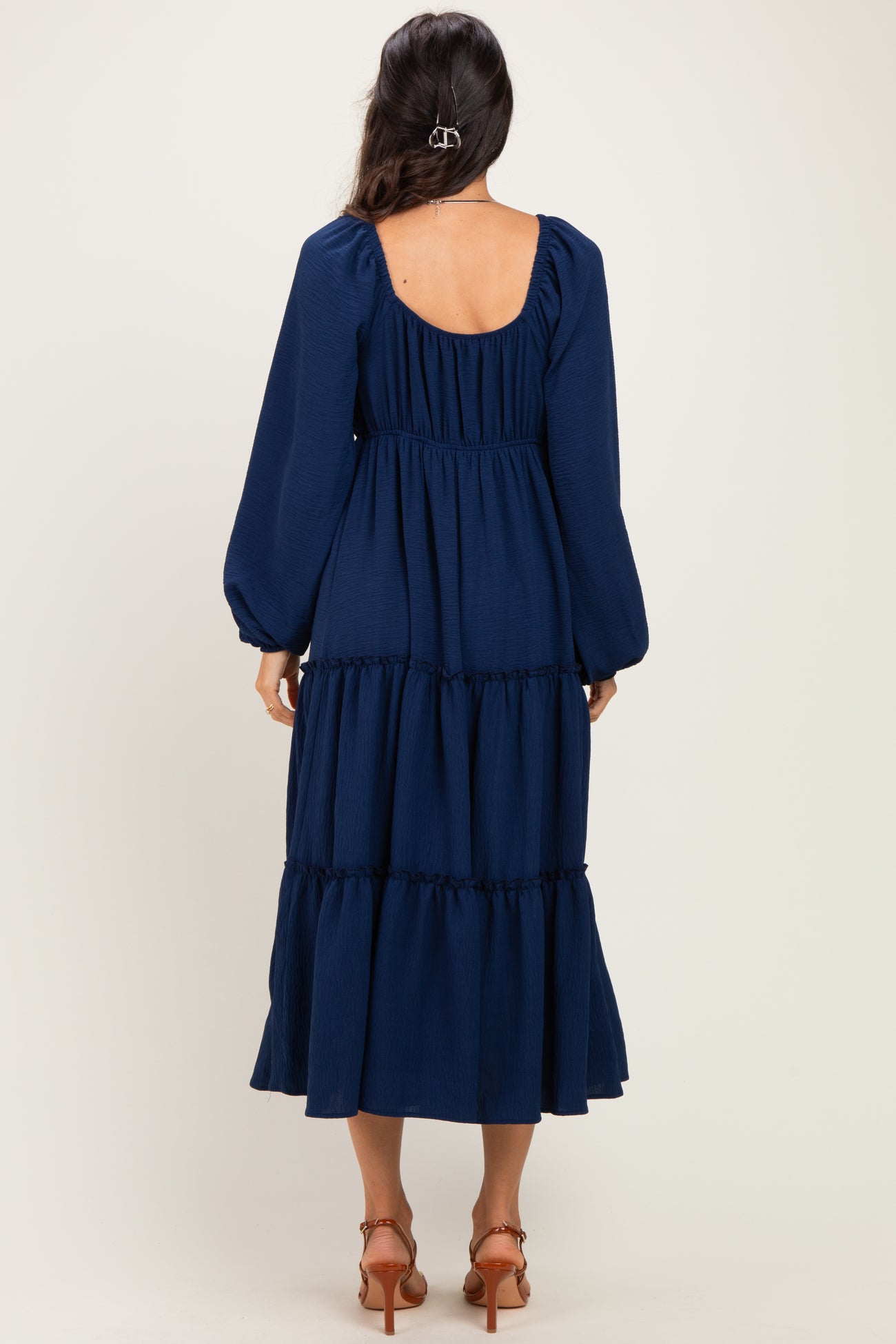 woman wearing a navy blue tiered maxi dress with long puff sleeves and a scoop back