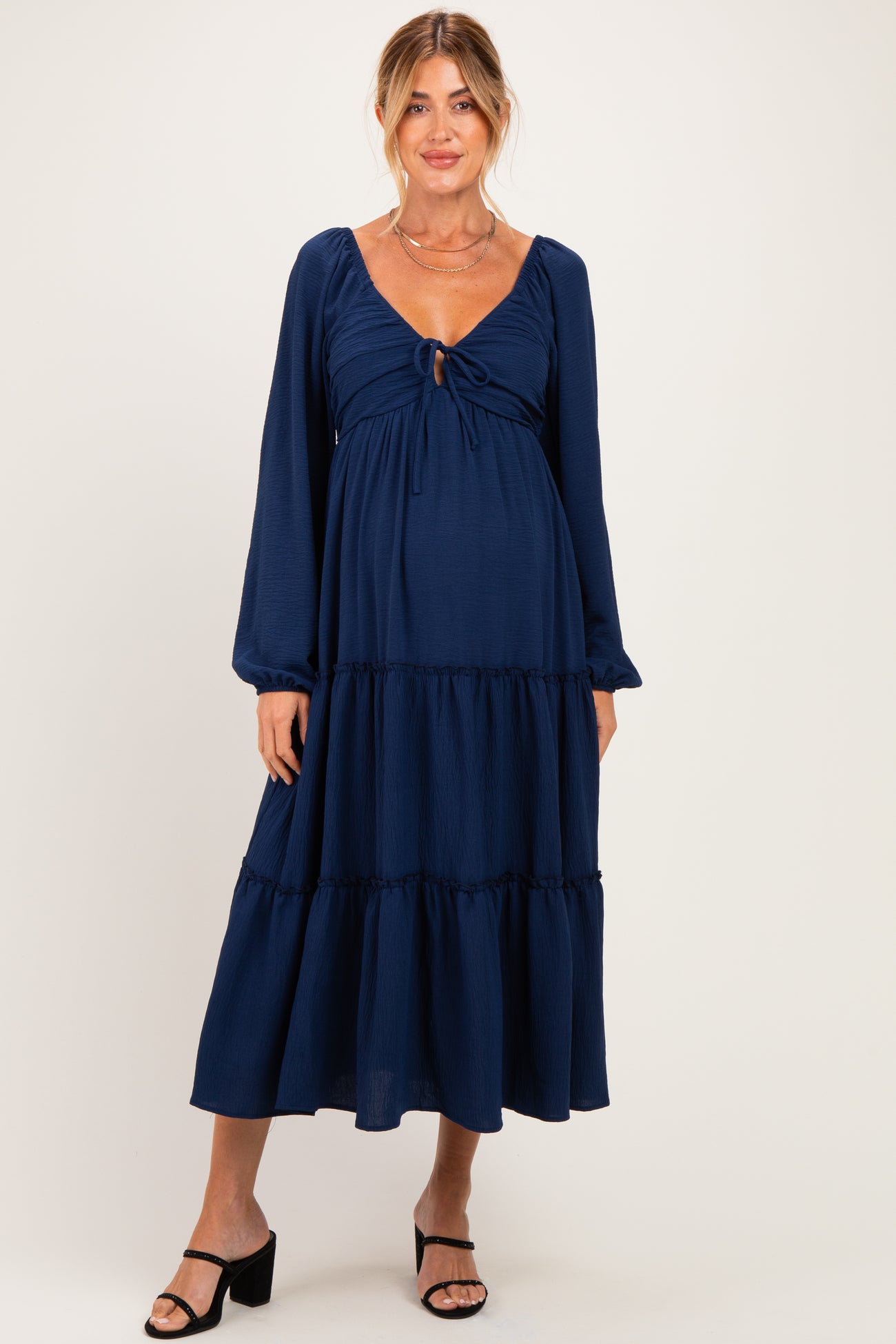 woman wearing a navy blue tiered maternity dress with long sleeves and a tie front detail, showcasing a baby bump
