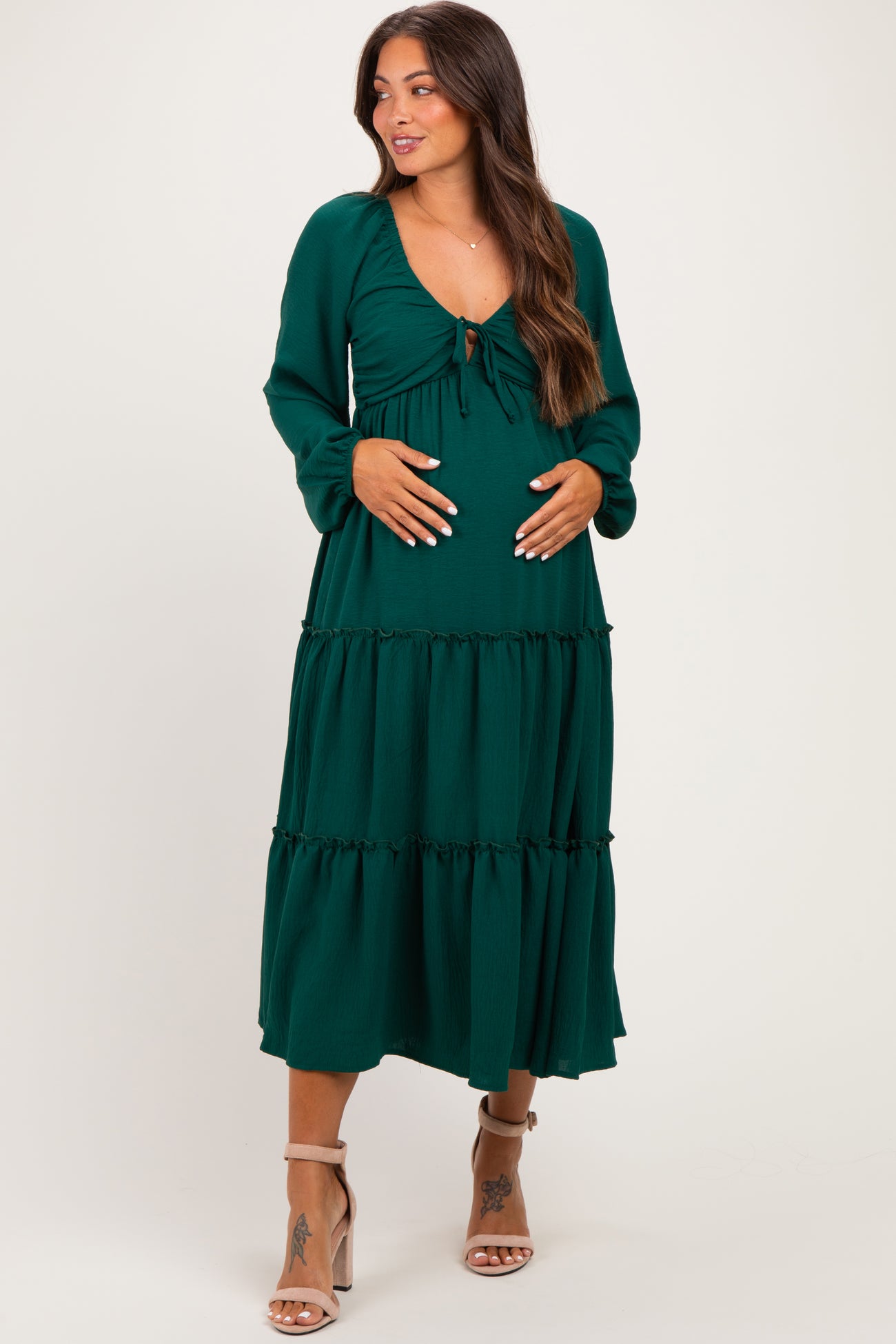 woman wearing a dark green maternity dress with a tie front and tiered skirt, holding her baby bump