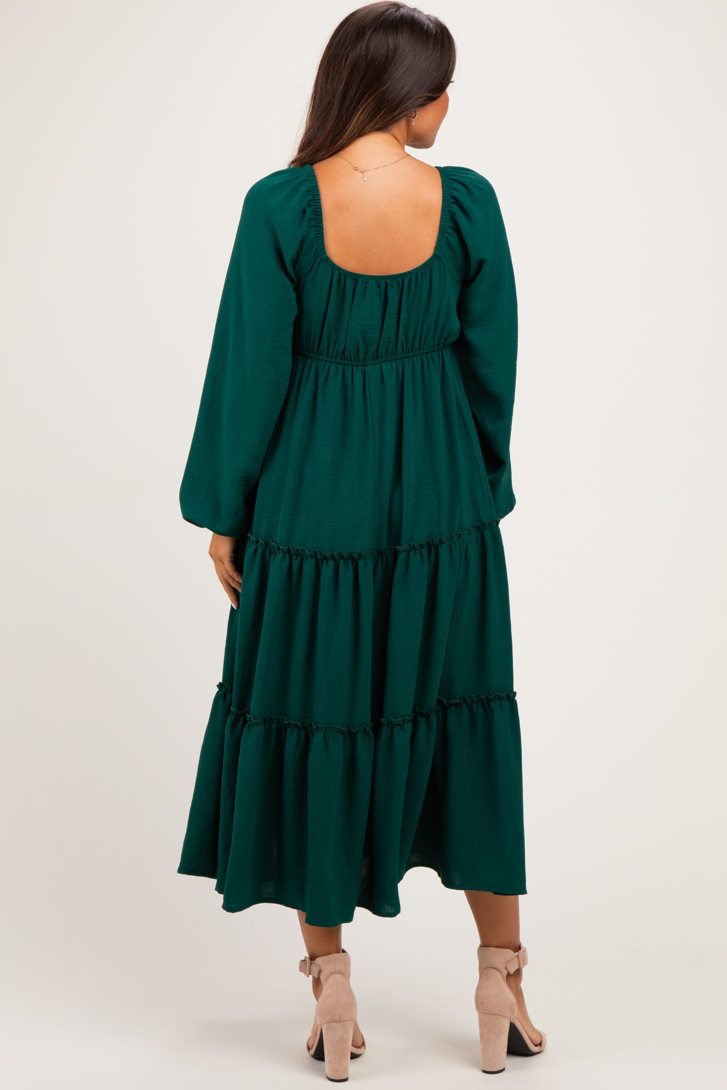 woman wearing a dark green maternity dress with long sleeves and tiered skirt, showing a scooped back design