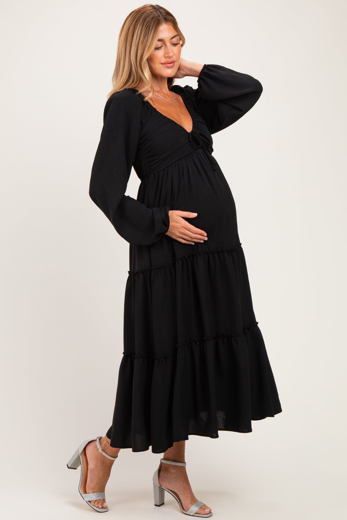 woman wearing a black tiered maternity dress with long sleeves and a baby bump visible, posing gracefully