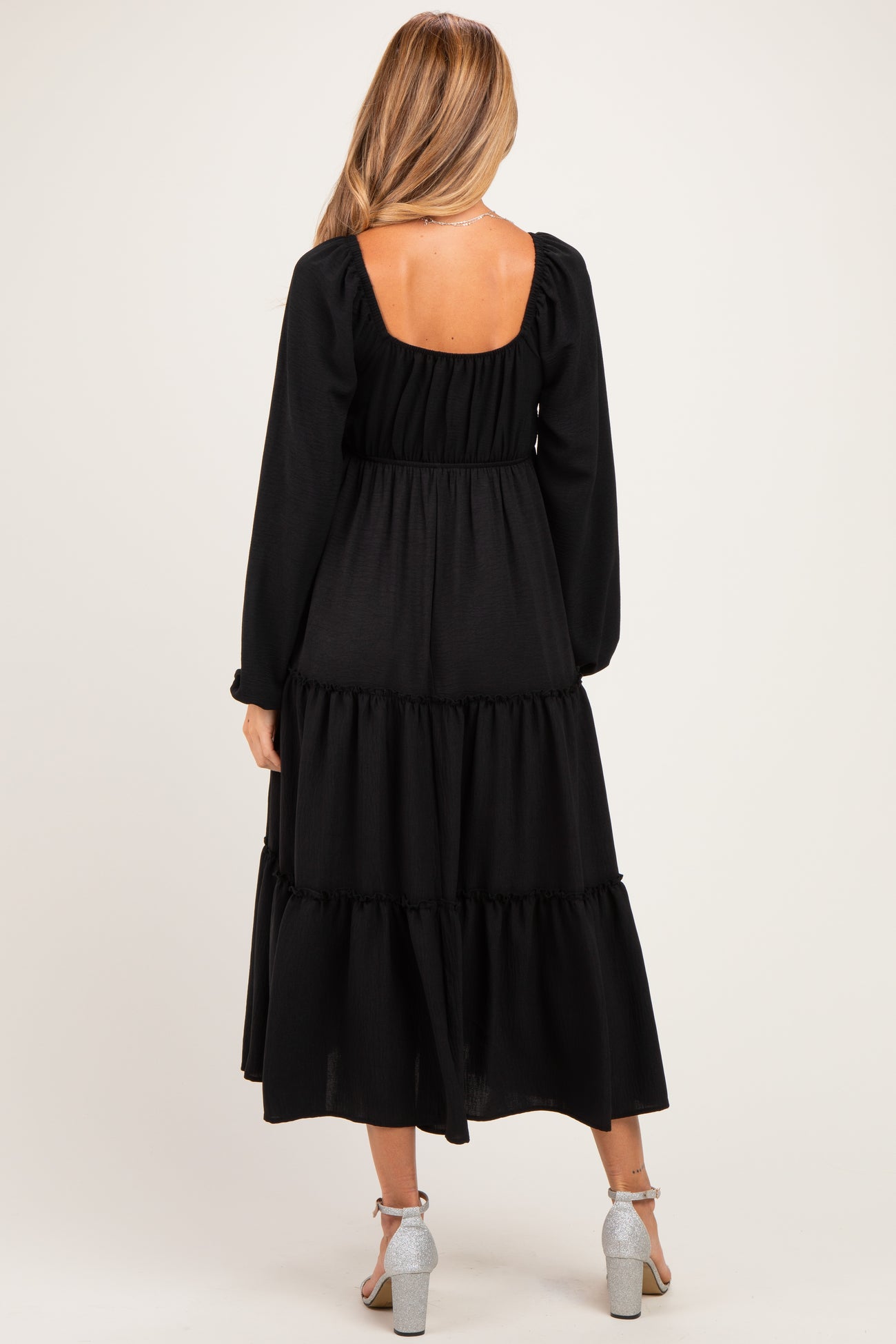 woman wearing a black tiered maternity dress with long sleeves and a square back design