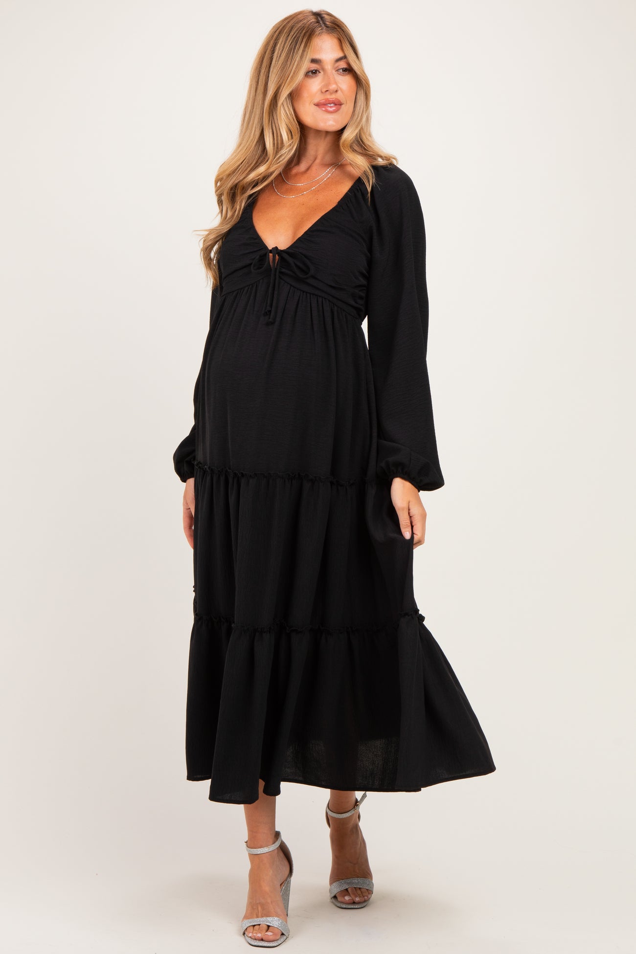 woman wearing a black maternity dress with a tie front and long sleeves, showcasing her baby bump