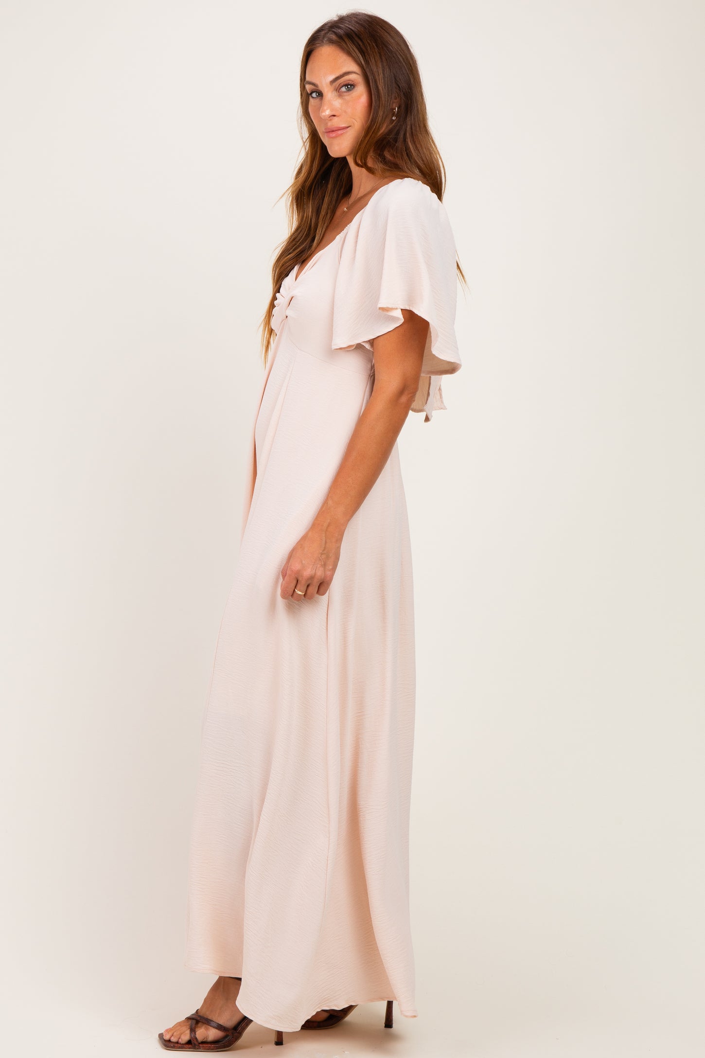 woman wearing a soft pink maxi dress with flutter sleeves and a knot detail at the neckline