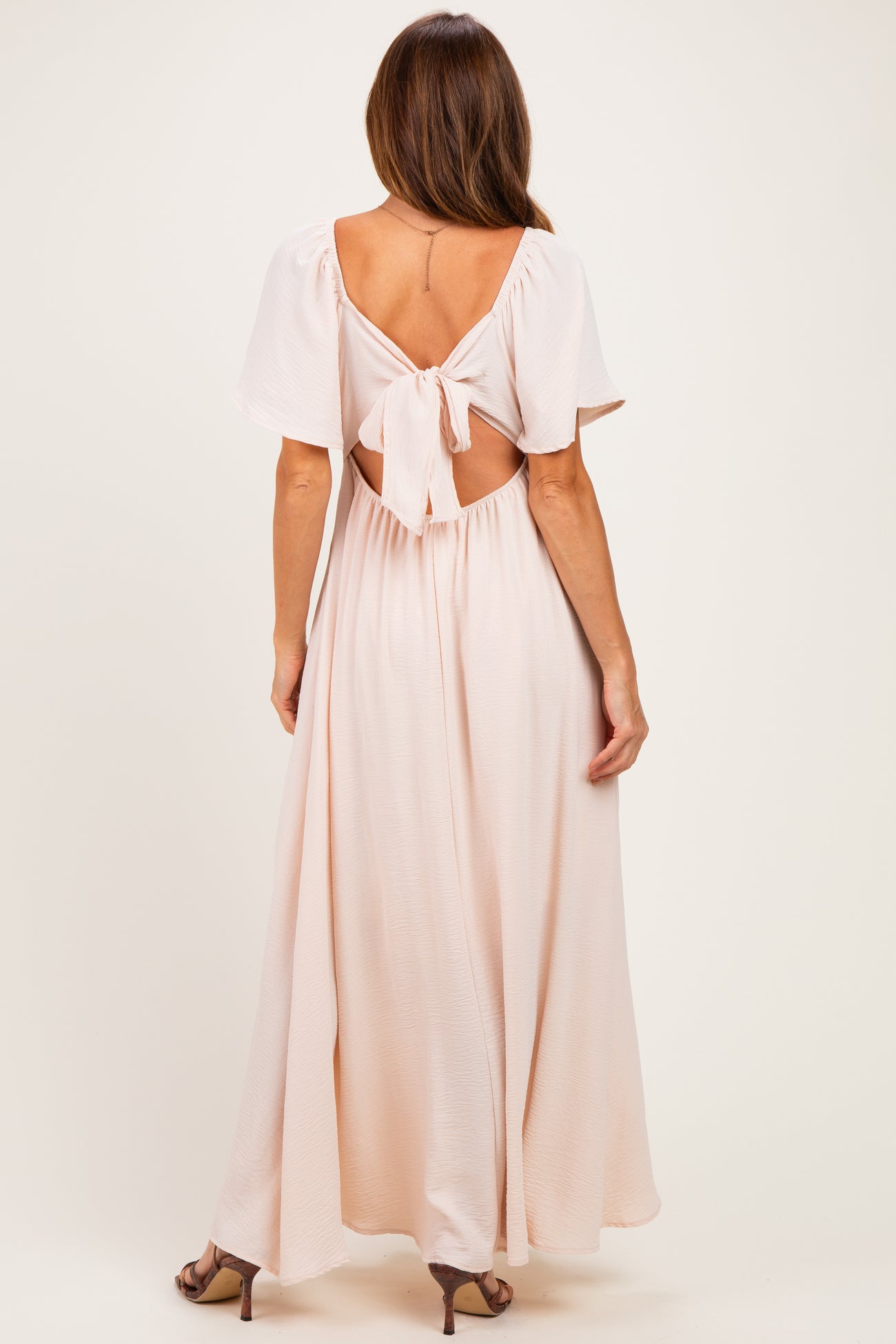 woman wearing a light pink maxi dress with a tie-back design and flutter sleeves