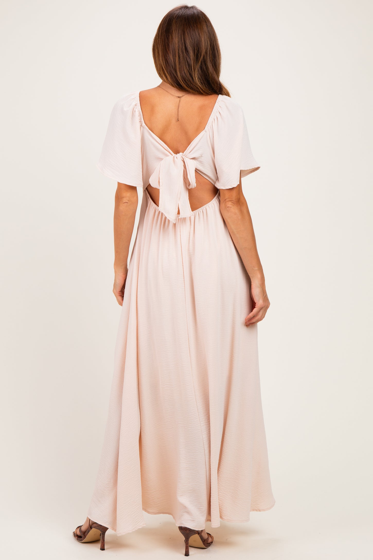 woman wearing a light pink maxi dress with a tie-back design and flutter sleeves