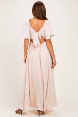 woman wearing a light pink maxi dress with a tie-back design and flutter sleeves