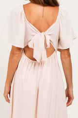 woman wearing a light pink backless dress with flutter sleeves and a bow tie detail at the back