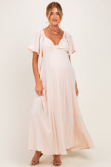 woman wearing a light pink maternity maxi dress with flutter sleeves and a scoop neckline, showing her baby bump