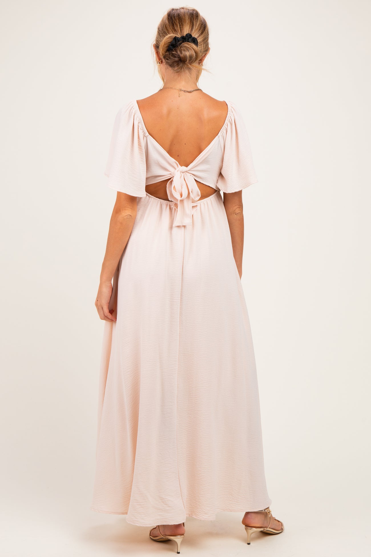 woman wearing a blush pink maternity maxi dress with a back tie detail and short flutter sleeves