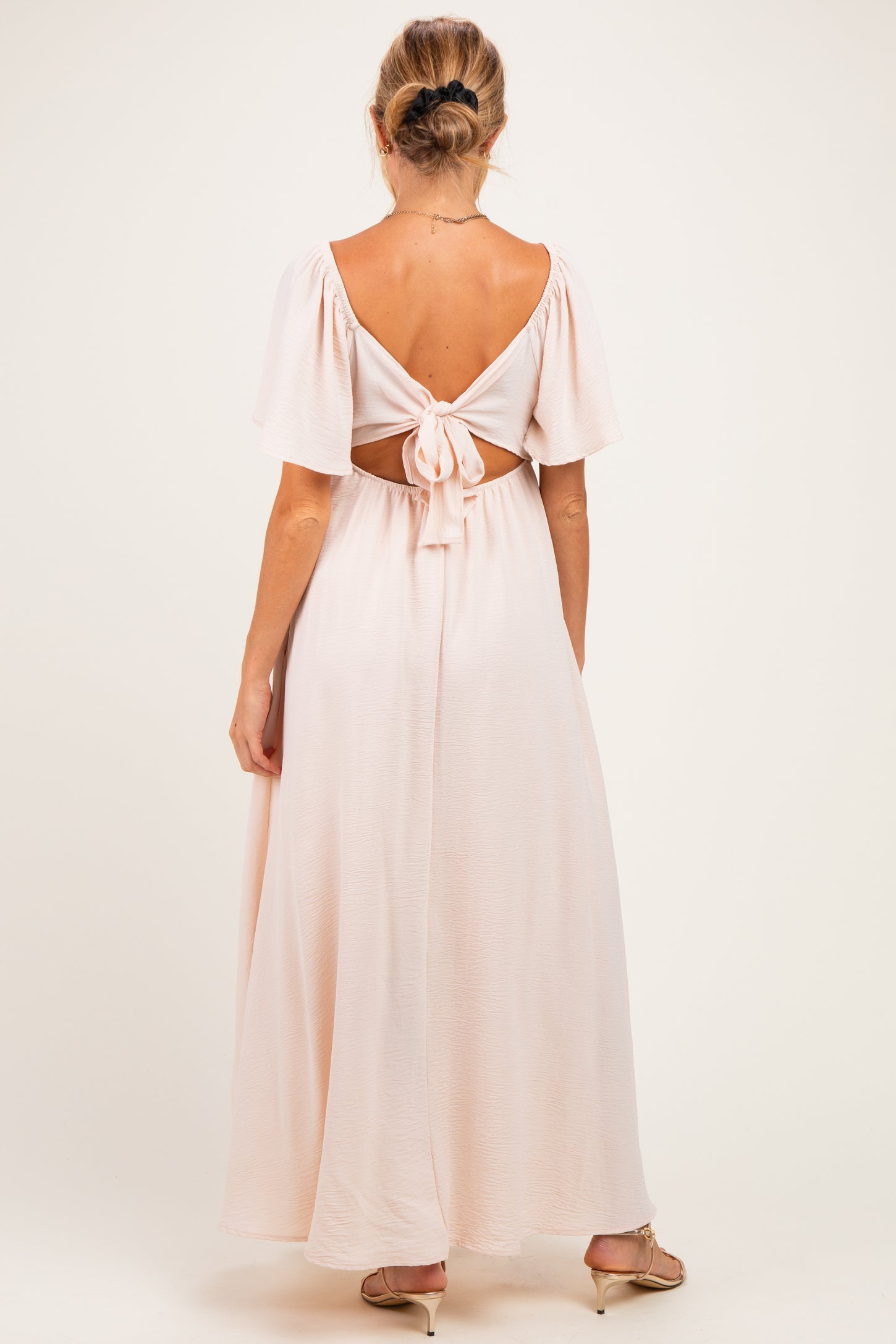 woman wearing a blush pink maternity maxi dress with a back tie detail and short flutter sleeves