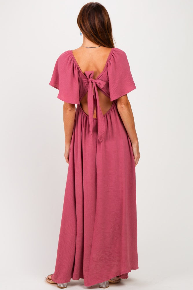 woman wearing a dusty rose maxi dress with flutter sleeves and an open back with a tie detail