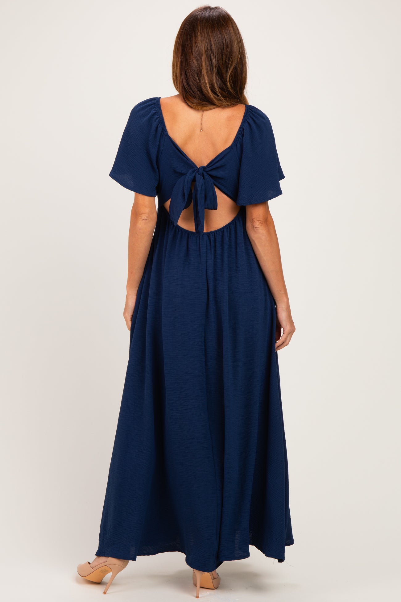 woman wearing a dark navy blue maxi dress with a tied open back and flutter sleeves