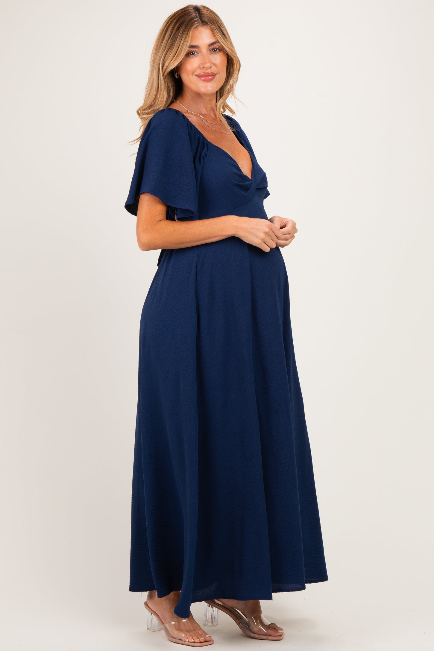 woman wearing a navy blue maxi maternity dress with short flutter sleeves and a v-neck, showing her baby bump