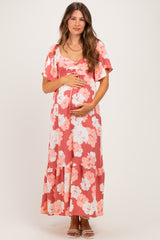 woman wearing a pink floral maternity maxi dress and cradling her baby bump