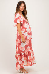 woman wearing a coral floral maternity maxi dress with short sleeves and a ruffled hem, showcasing a baby bump