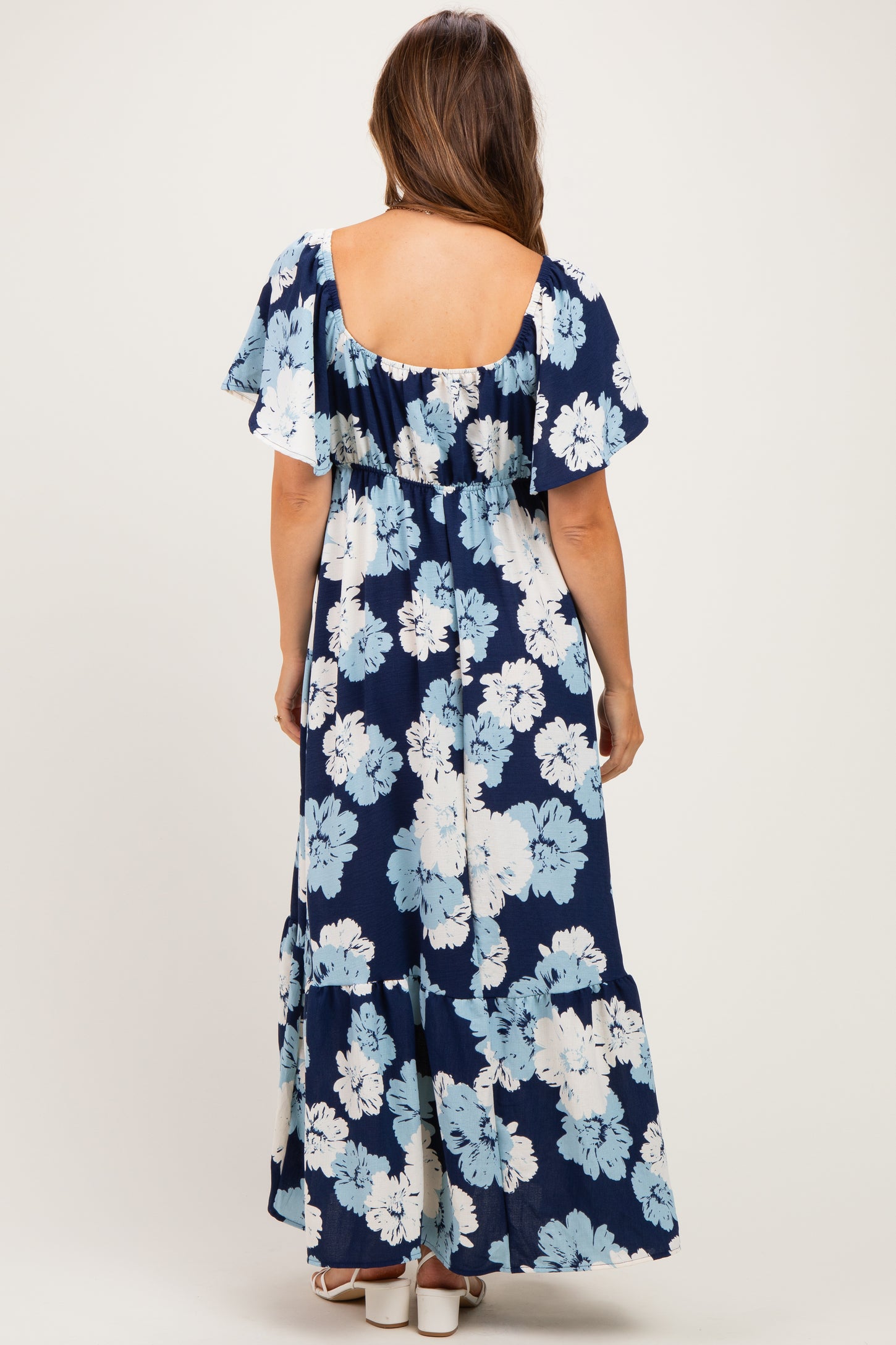 woman wearing a navy blue floral maternity maxi dress with short flutter sleeves and an open back