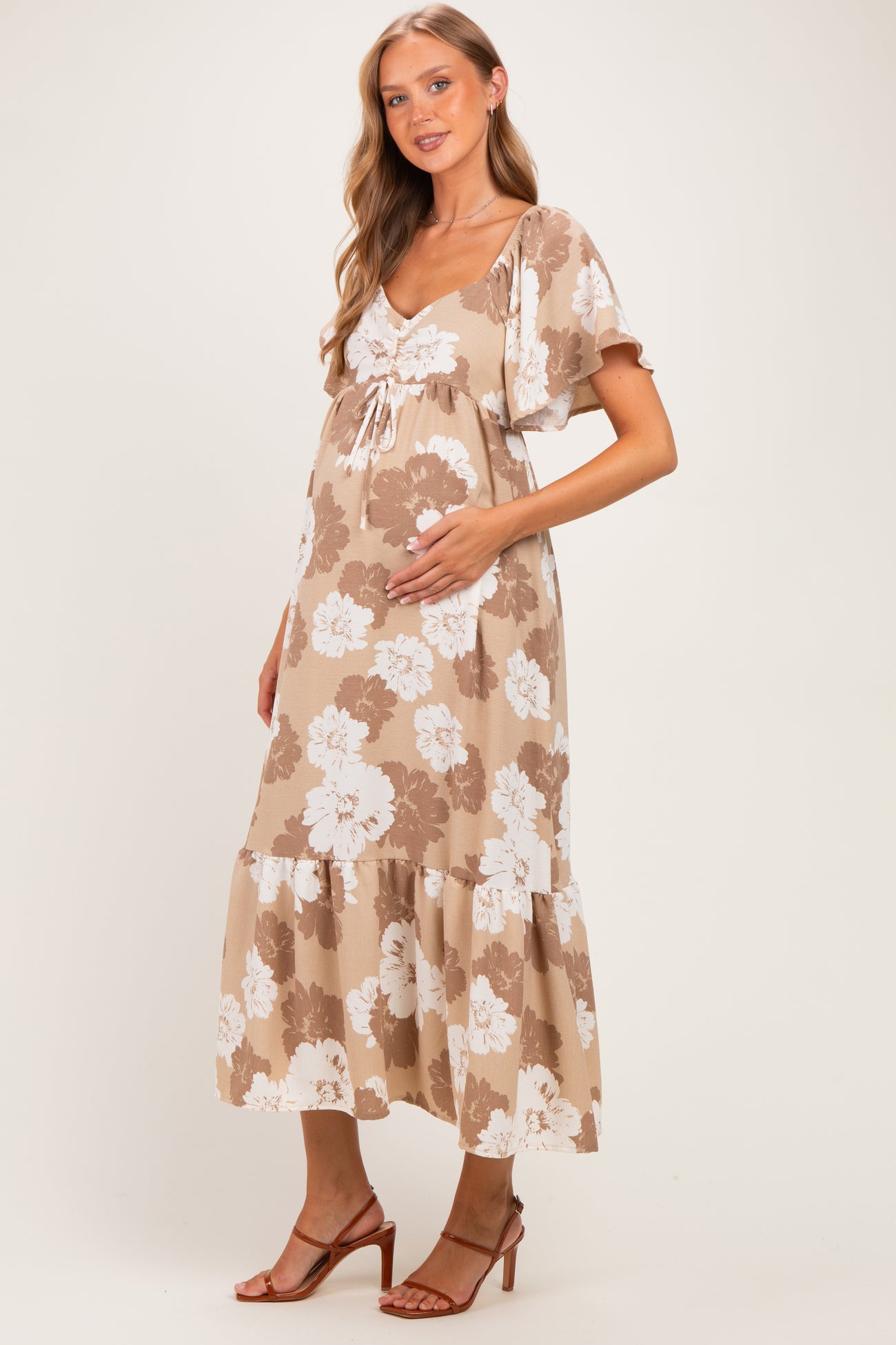 woman wearing a floral beige maternity dress with a tiered skirt and holding her baby bump