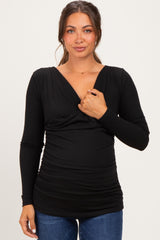 woman wearing a black long sleeve maternity top with a deep v-neck and ruched sides, showing her baby bump