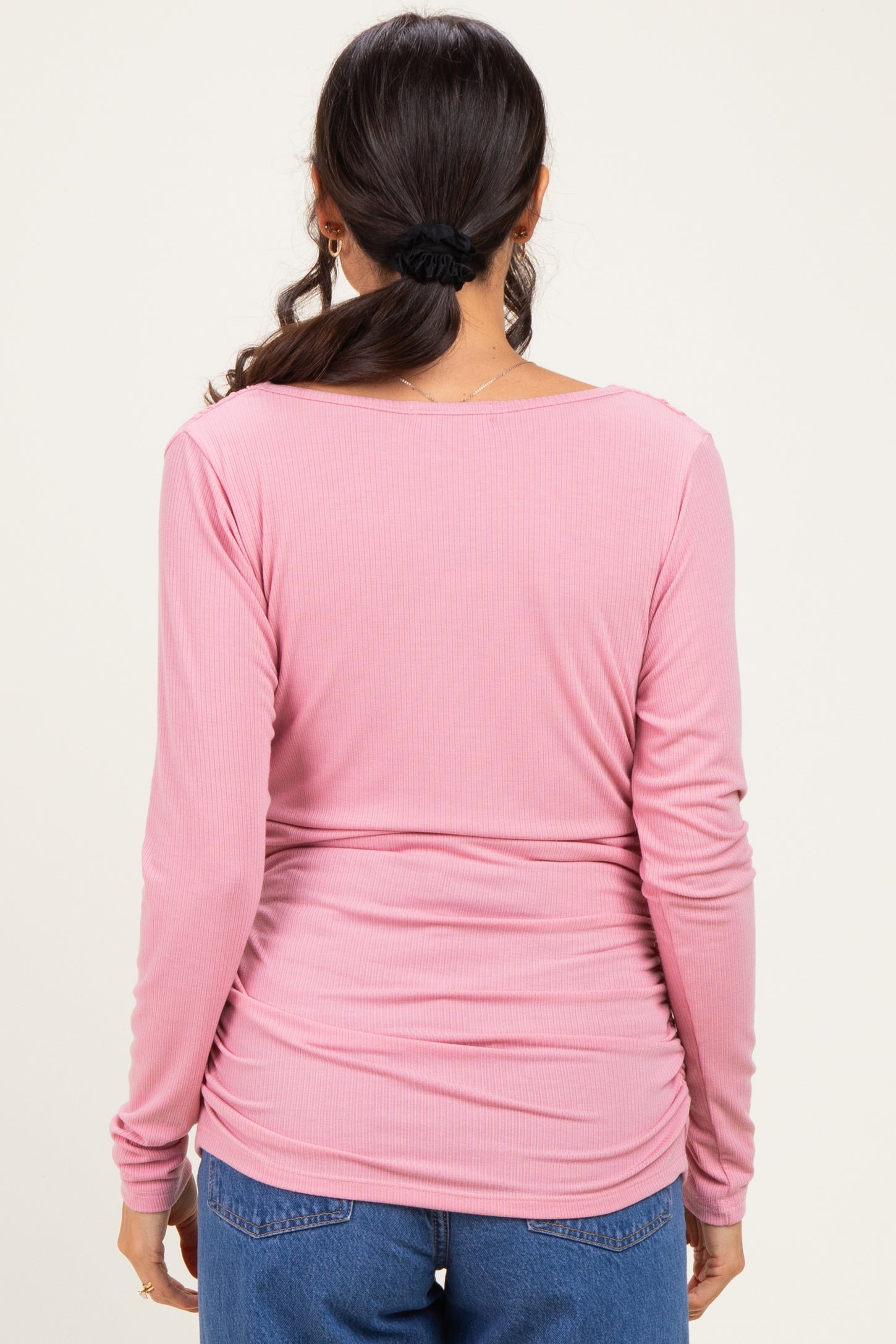 woman wearing a pink long sleeve fitted top with a scooped back and ruching detail, seen from the back