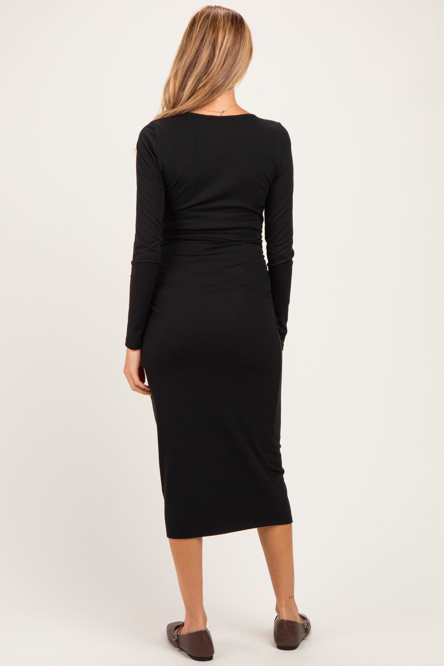 woman wearing a black ribbed maternity dress, showing a fitted silhouette and long sleeves, with the back view visible