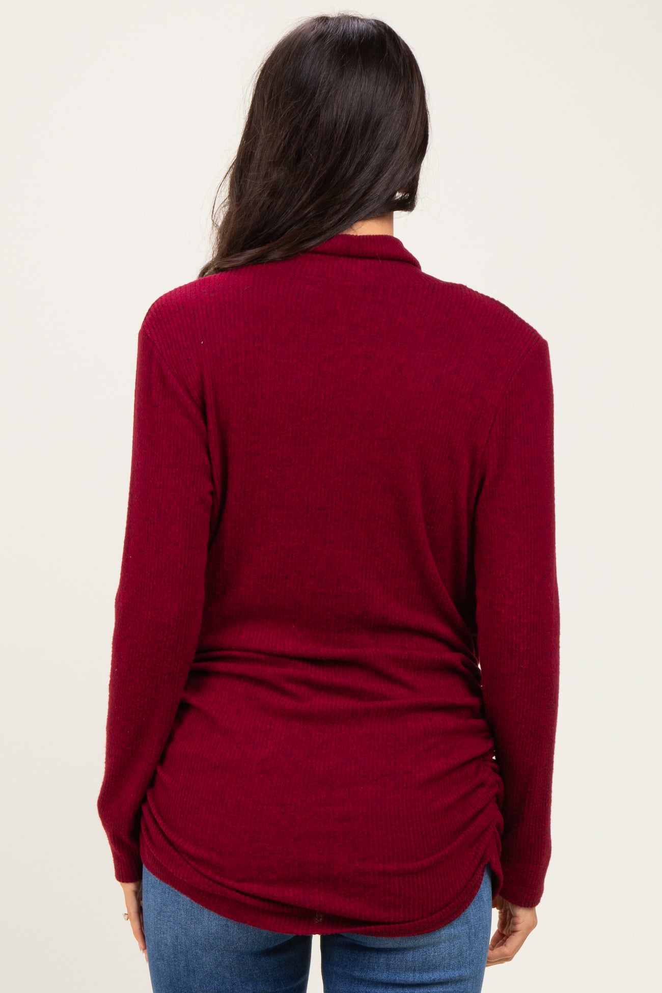 woman wearing a burgundy long sleeve top with a gathered back detail and paired with blue jeans