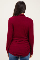 woman wearing a burgundy long sleeve top with a gathered back detail and paired with blue jeans
