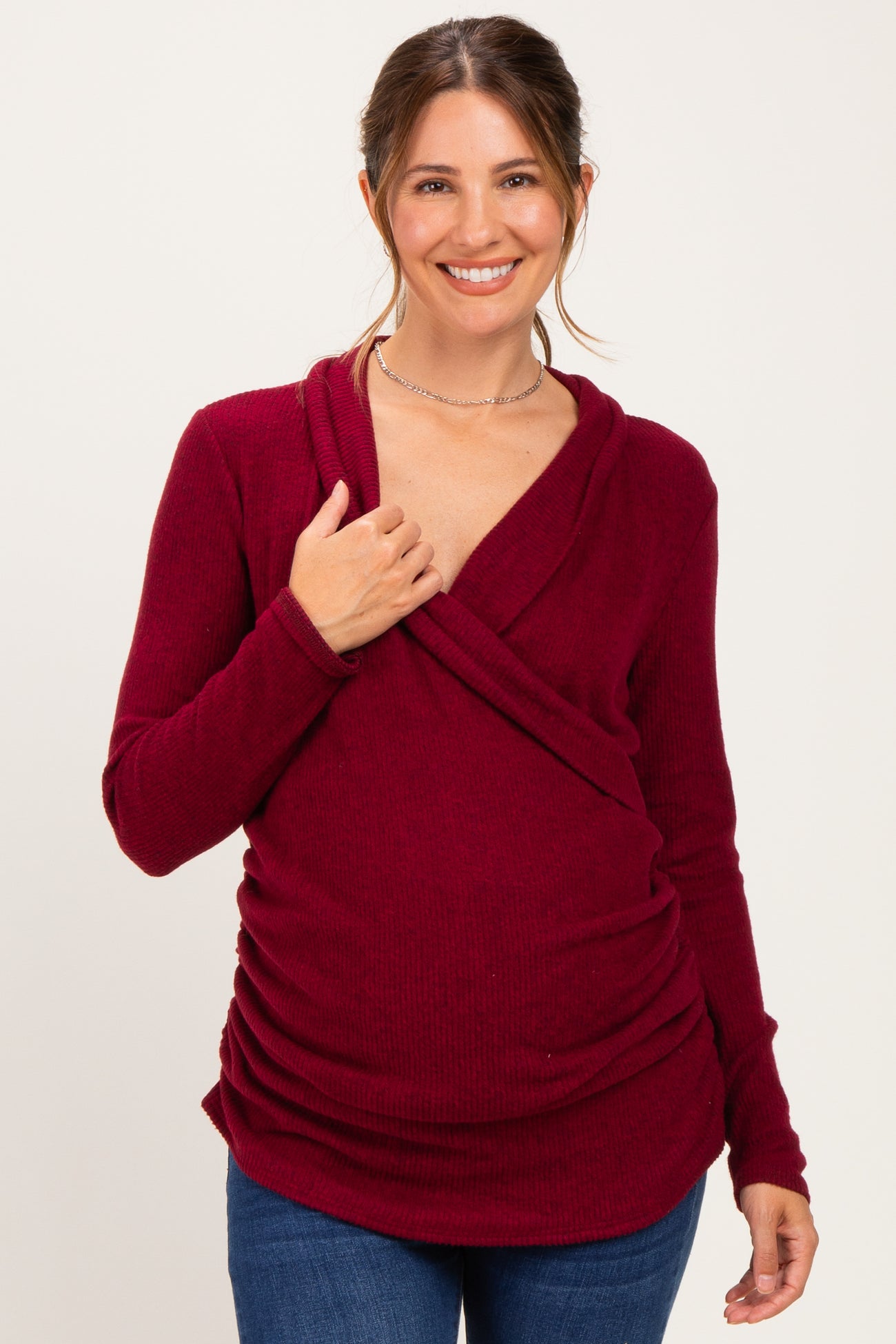 woman wearing a burgundy maternity wrap top with gathered detailing, smiling and holding her baby bump