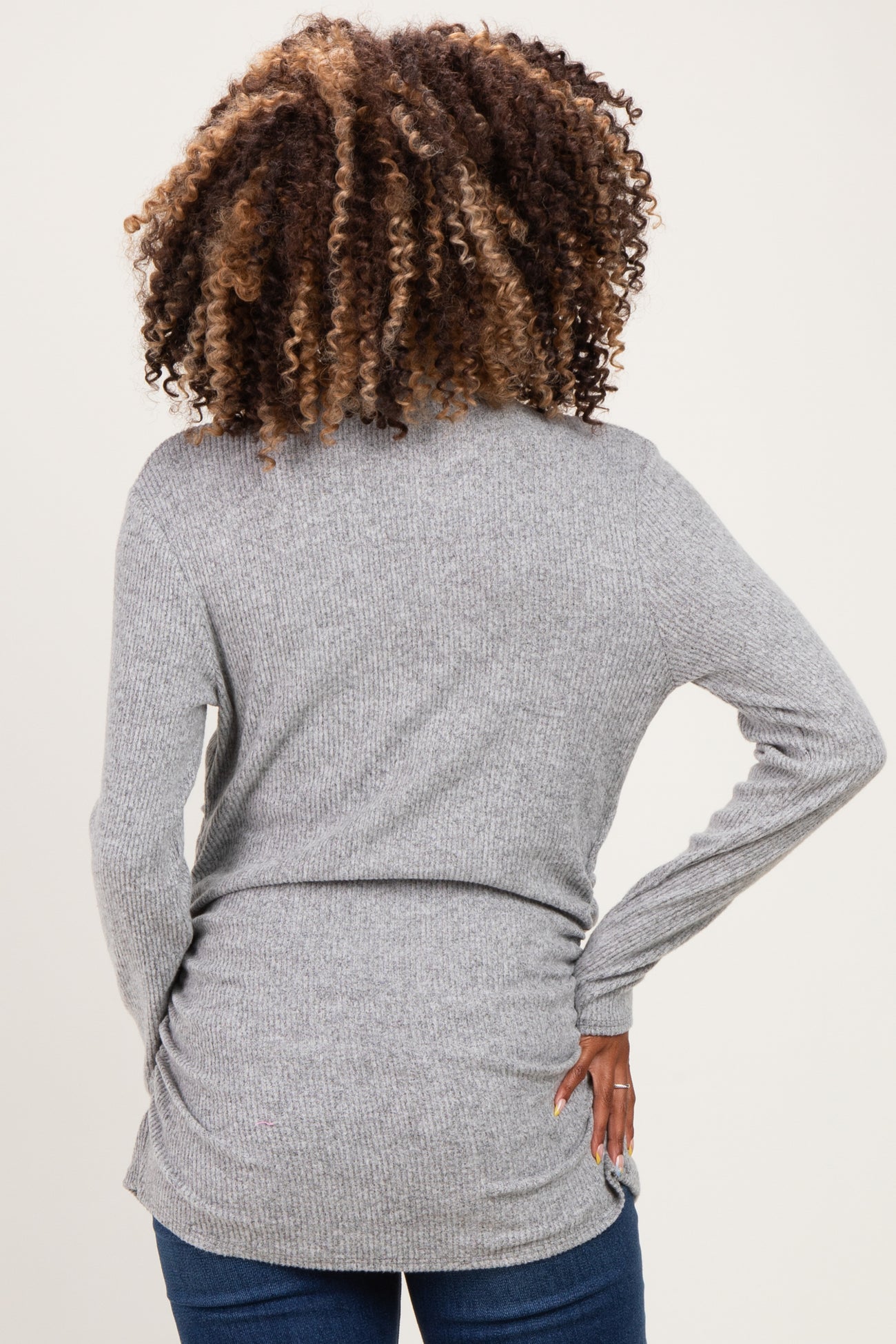 woman wearing a gray maternity sweater with a fitted silhouette, showing the back view and styled with loose curls
