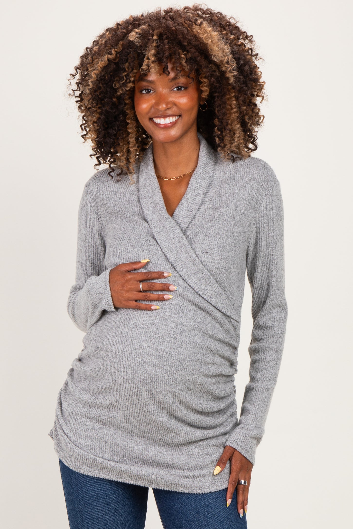 woman wearing a gray wrap maternity sweater and holding her baby bump