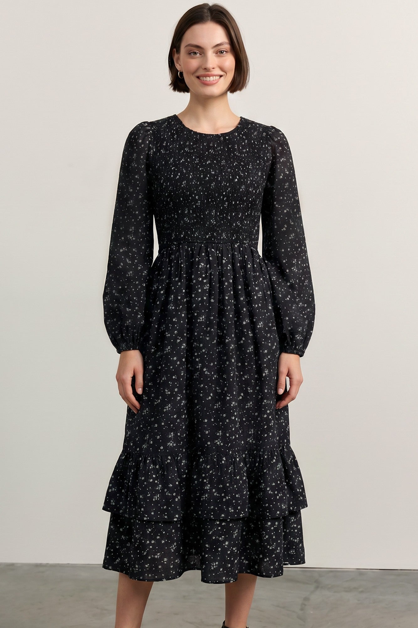 woman wearing a black floral long sleeve dress with a smocked bodice and tiered ruffle hem