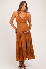woman wearing a rust-colored maternity dress with embroidered details and a baby bump, standing and holding her belly