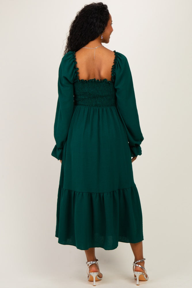 woman wearing a green maternity dress with a smocked bodice and long sleeves, showcasing a tiered skirt from the back