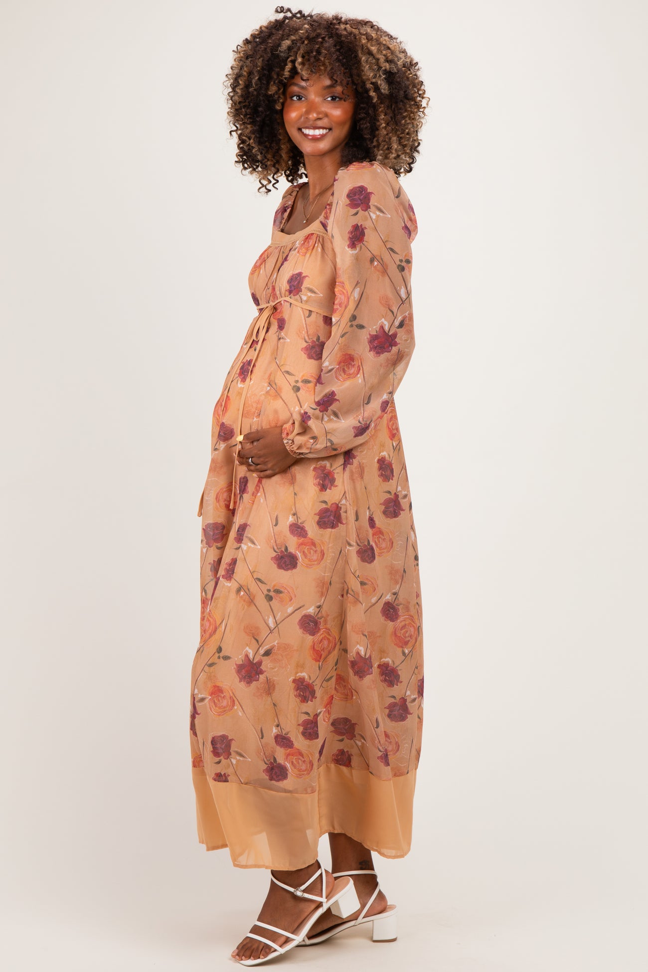 woman wearing a floral maternity maxi dress with long sleeves and a tied waist, holding her baby bump