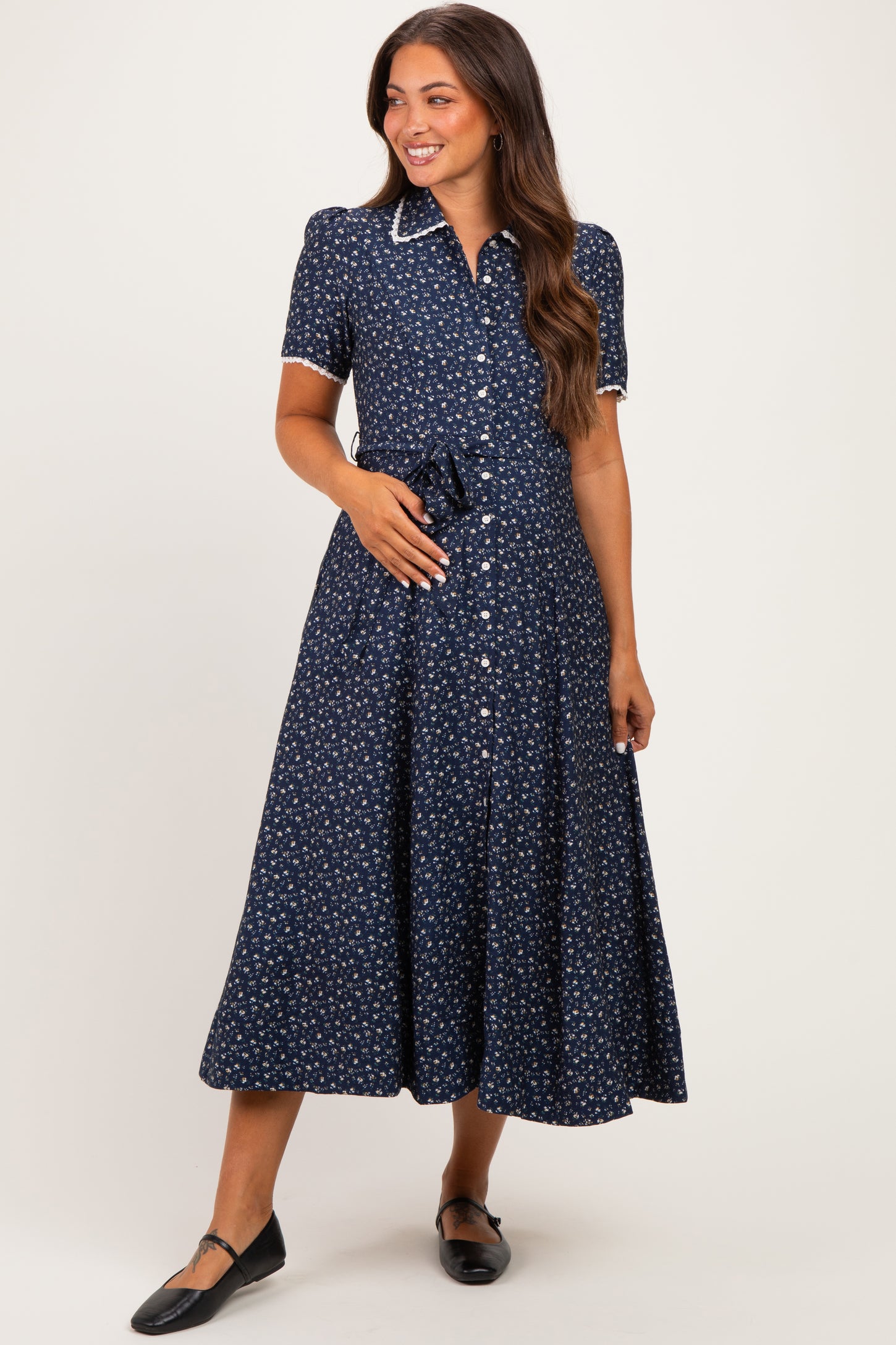 woman wearing a navy blue floral maternity dress with short sleeves and a tie waist, showcasing her baby bump