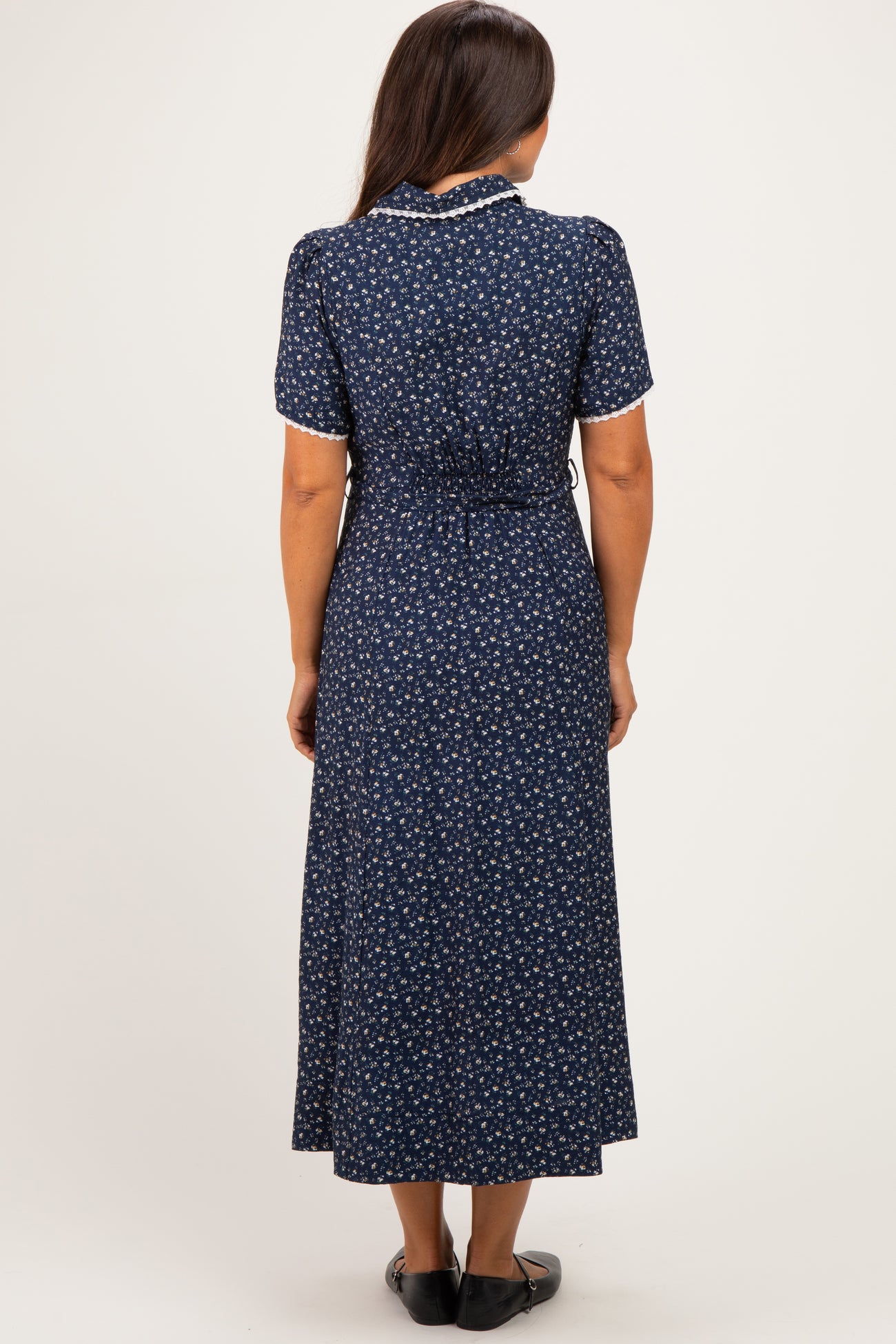 woman wearing a navy blue floral short sleeve maternity dress with a tied waist detail, showing a baby bump from behind