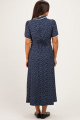 woman wearing a navy blue floral short sleeve maternity dress with a tied waist detail, showing a baby bump from behind