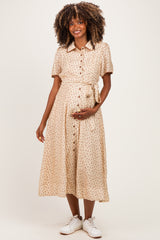 woman wearing a beige floral midi maternity dress with buttons and a tie waist, holding her baby bump
