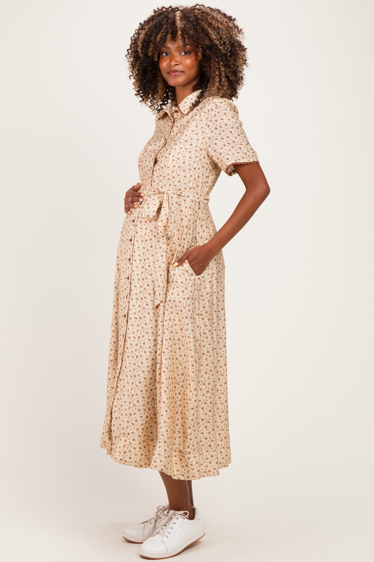 woman wearing a beige floral maternity dress with short sleeves and a tie waist, showing her baby bump